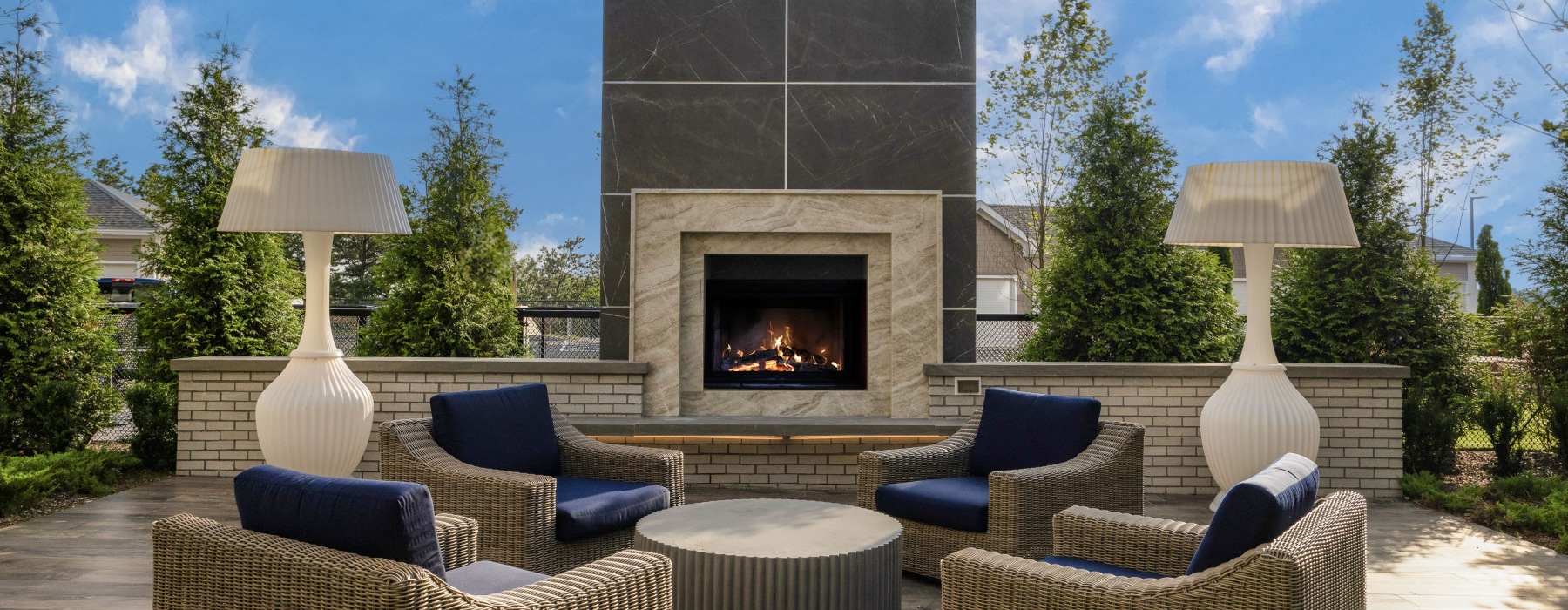 outdoor fireplace with large decorative white lamps and 4 cushioned outdoor armchairs and coffee table